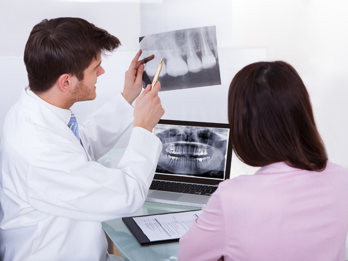 Dentist explaining dental X-rays to a patient using both film and a digital image on a laptop