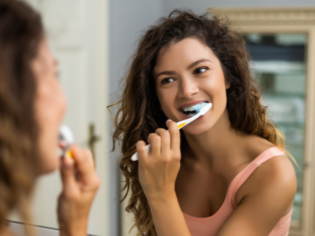 Young woman brushing her teeth while smiling in front of a mirror