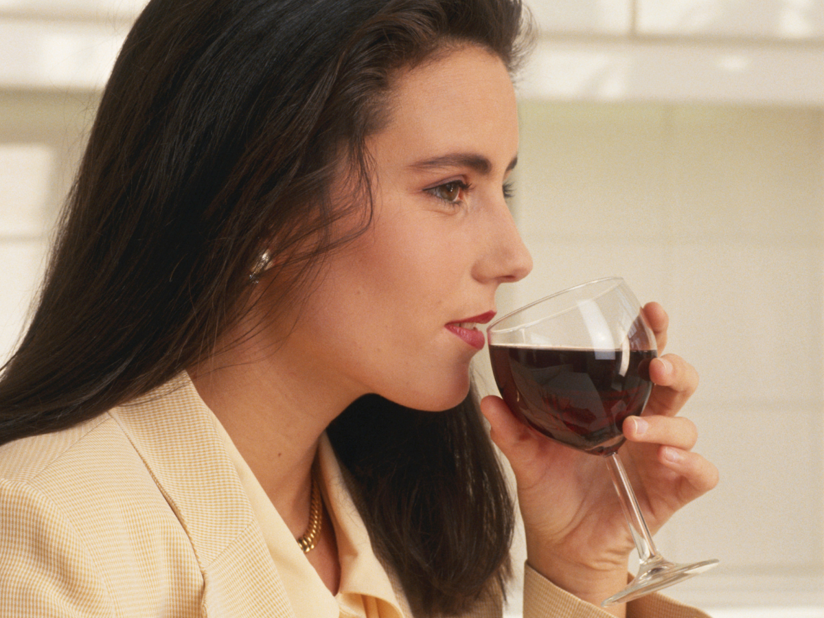 Woman sipping red wine from a glass, close-up profile view