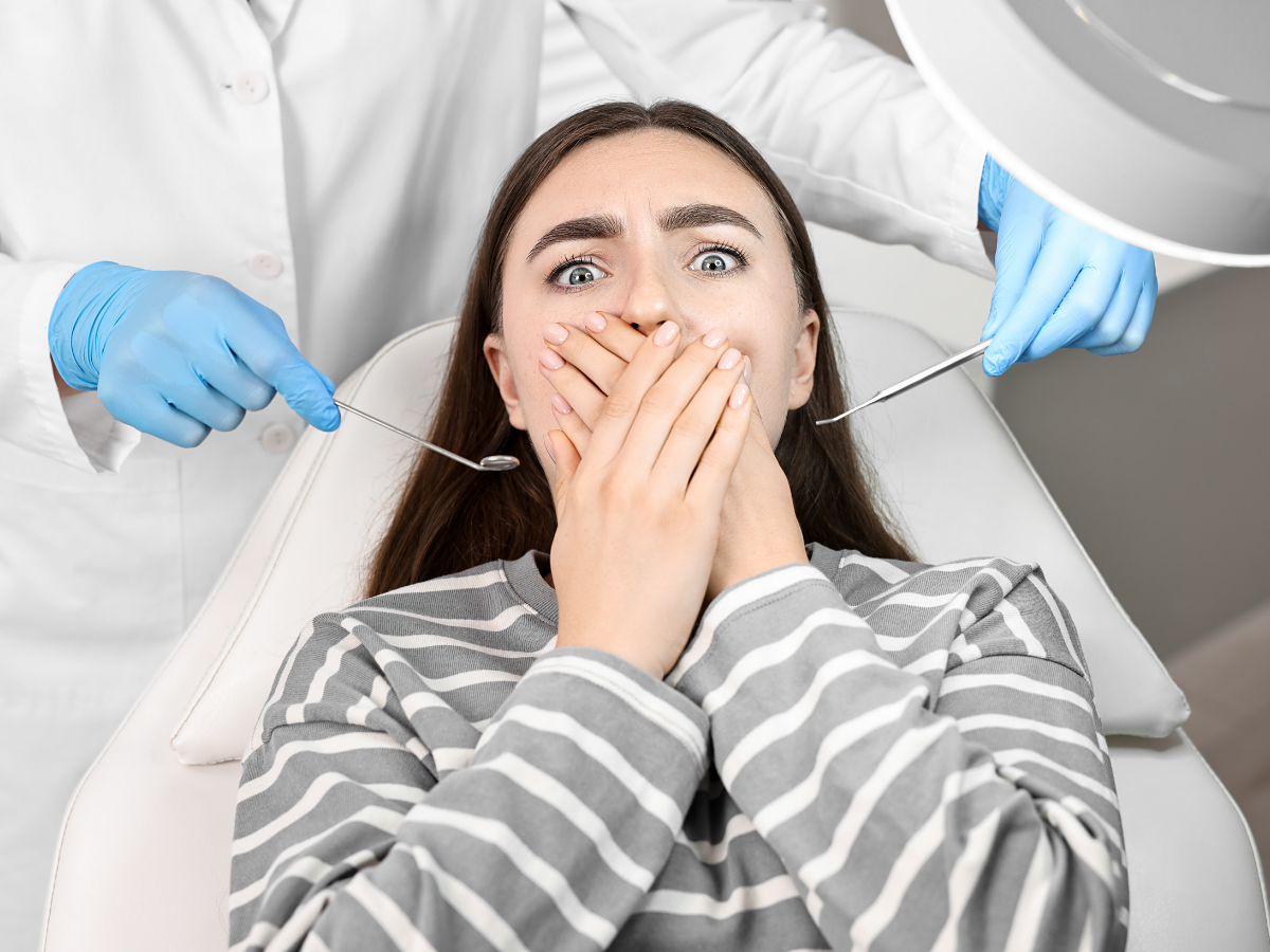 Anxious woman covering her mouth in a dental chair with dentist holding tools