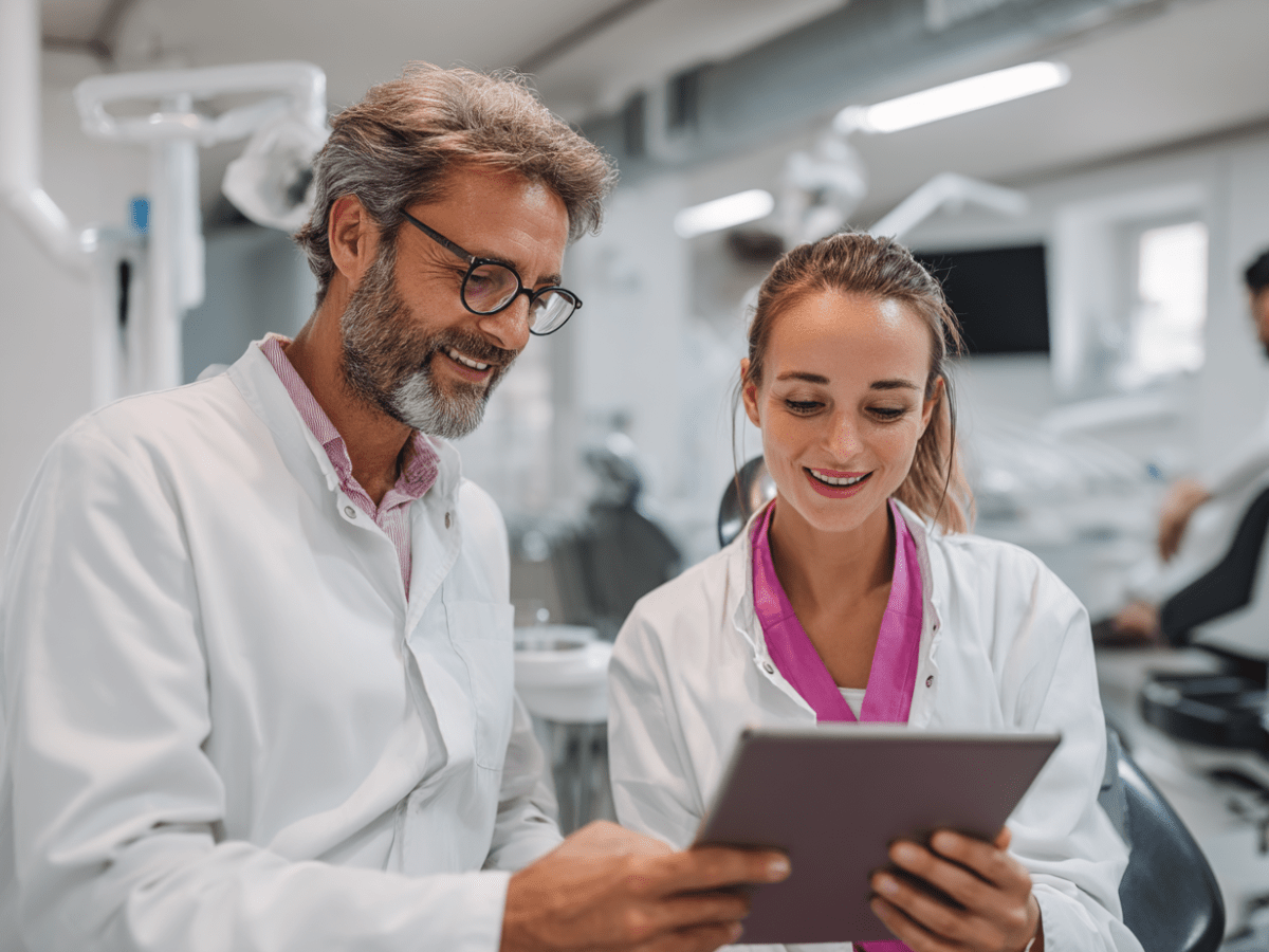 Two smiling dentists in white coats discussing patient care while reviewing information on a digital tablet inside a modern dental clinic