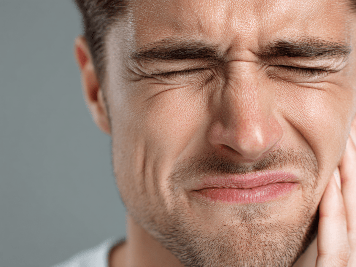 Close-up of a man with his eyes closed, clutching his jaw in discomfort due to TMJ disorder or jaw pain