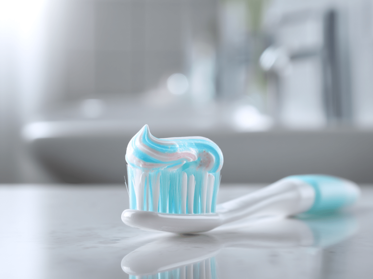Close-up of a white toothbrush with blue and white fluoride toothpaste on the bristles, placed on a bathroom counter