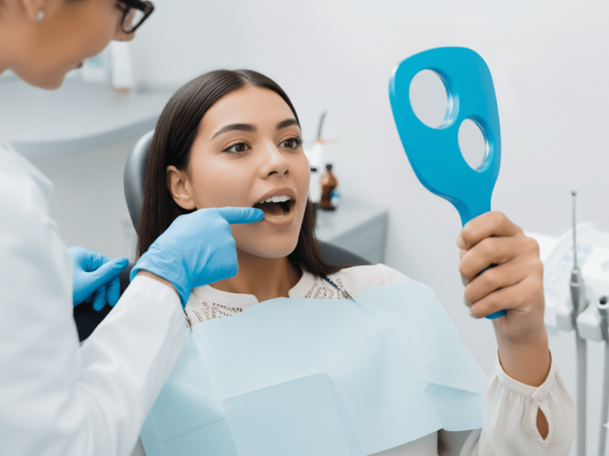 Dentist consultation with a female patient holding a mirror. The dentist is pointing to her teeth while discussing the treatment plan or dental procedure.