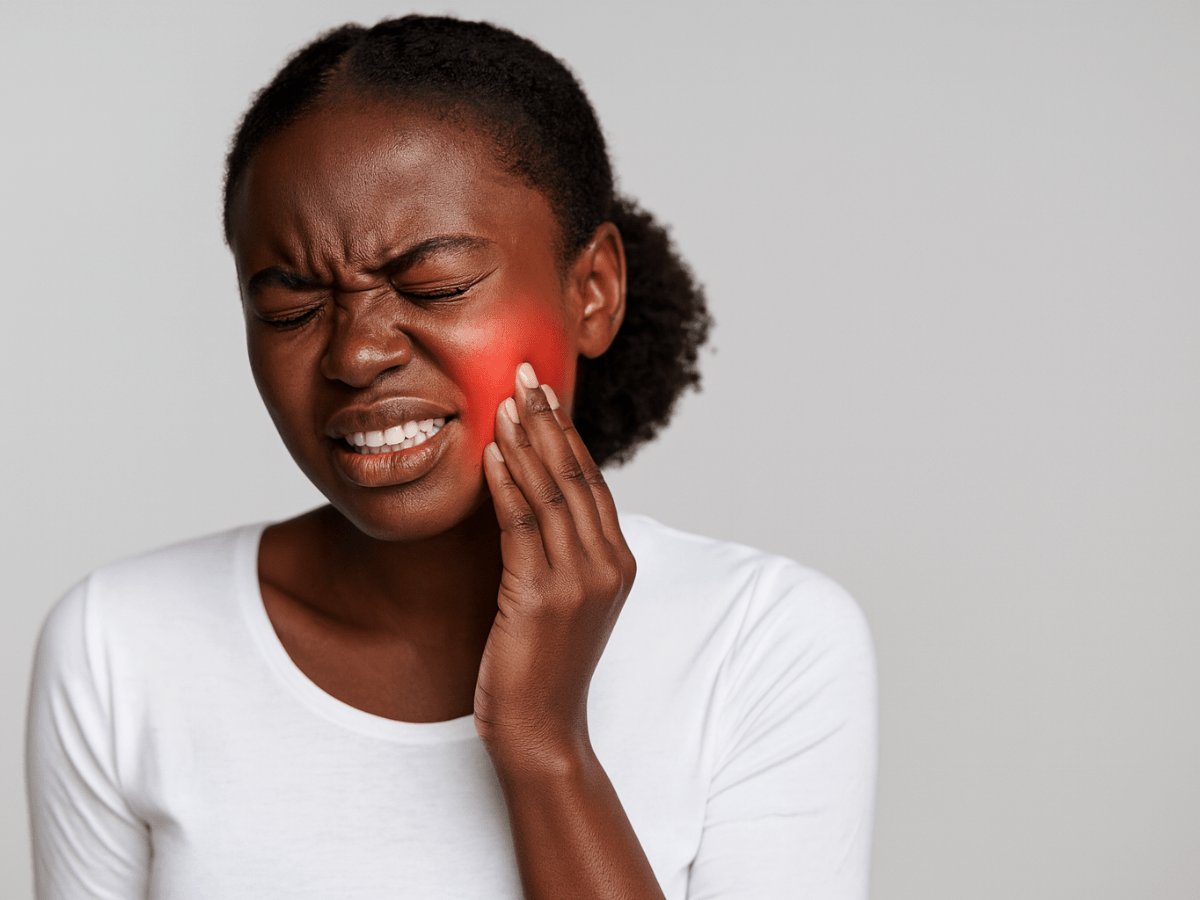 Frustrated young woman holding her cheek with a red highlight indicating severe toothache or dental pain, suggesting the need for an emergency dentist.