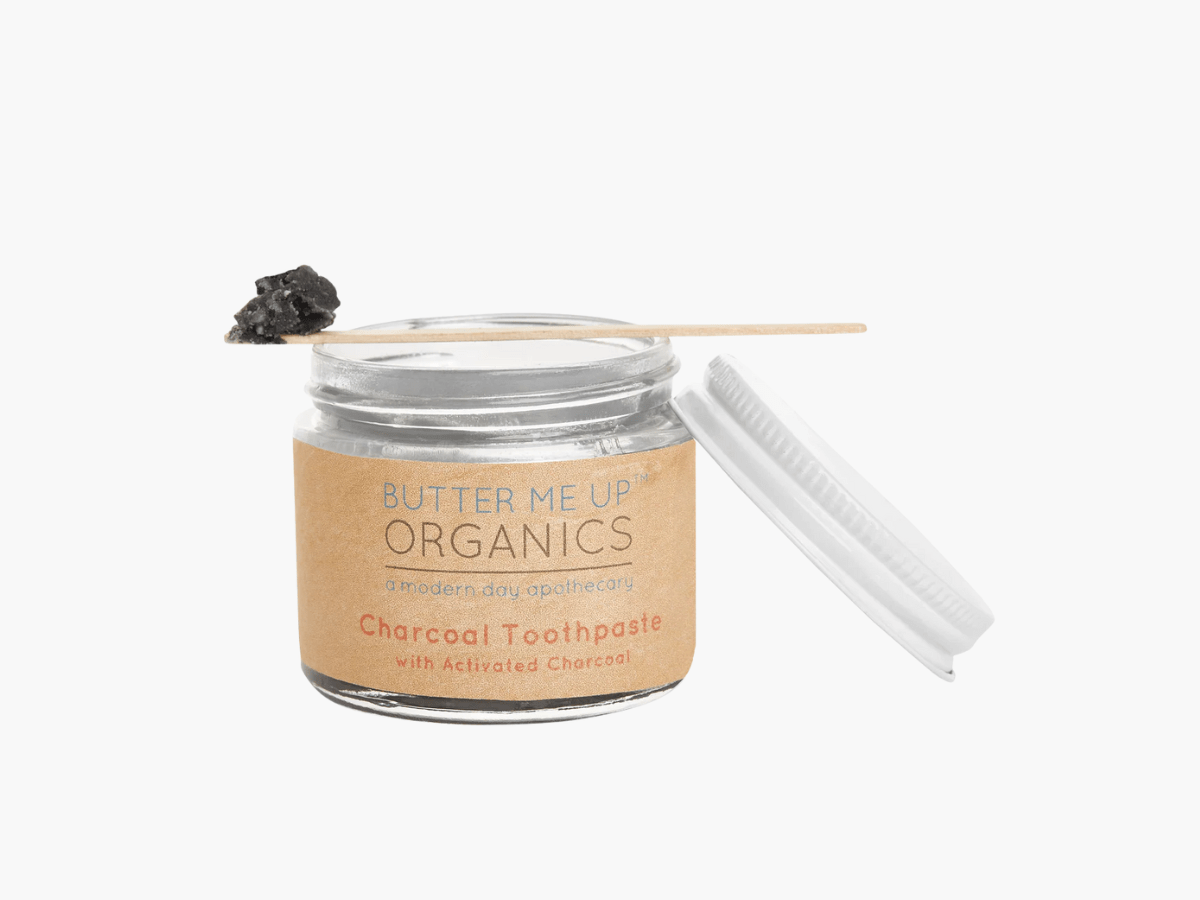 Butter Me Up Organics Toothpaste for Kids shown in a clear glass jar with a wooden applicator, highlighting natural, kid-safe ingredients and eco-friendly packaging.