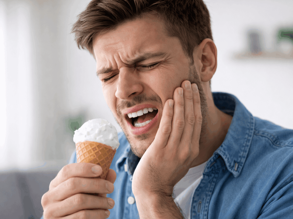 Man experiencing sharp tooth pain while eating ice cream, a common symptom of tooth sensitivity or enamel wear