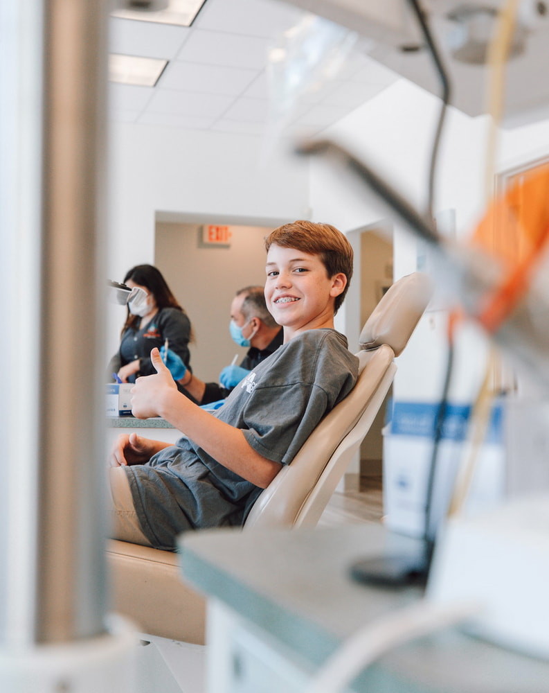 A cheerful boy seated in a dental chair, showing a bright smile while at the dentist's office. 