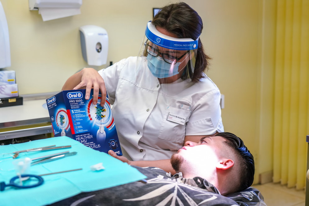 A woman in a dental office stands beside a man seated in a dental chair, preparing for a dental procedure. 