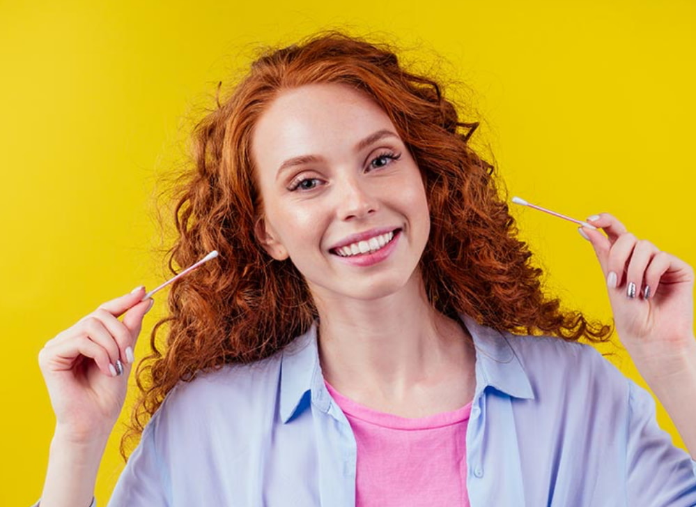 A woman with curly red hair smiles while holding a toothbrush in her right hand. 