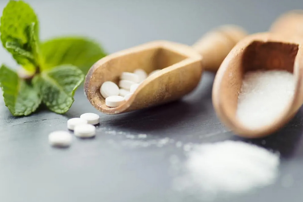 A wooden spoon holds sugar and salt, garnished with a fresh mint leaf, showcasing a contrast of flavors. 