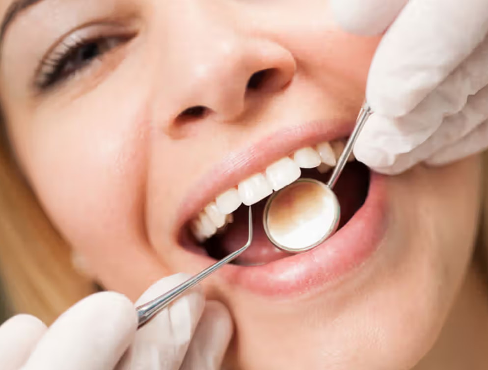 A woman sits in a dental chair while a dentist cleans her teeth with a dental tool. 