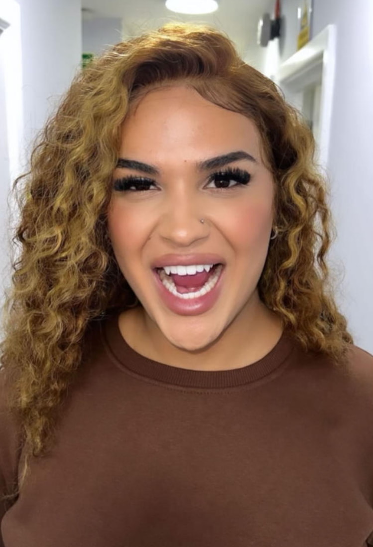 A woman with curly hair smiles warmly, showcasing her joyful expression. 