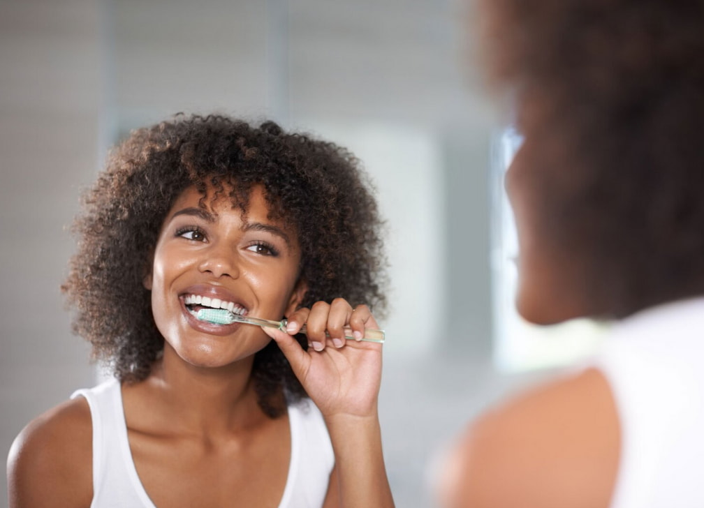 A woman brushing her teeth while looking into a bathroom mirror. 