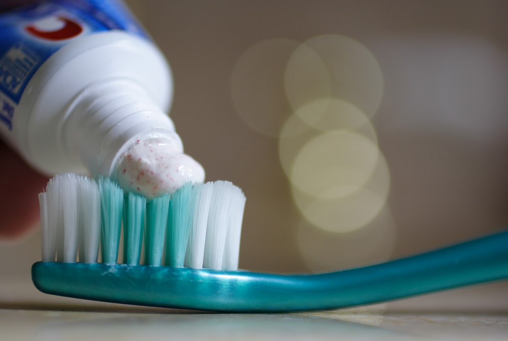 A person applying toothpaste onto a toothbrush in preparation for brushing their teeth. 