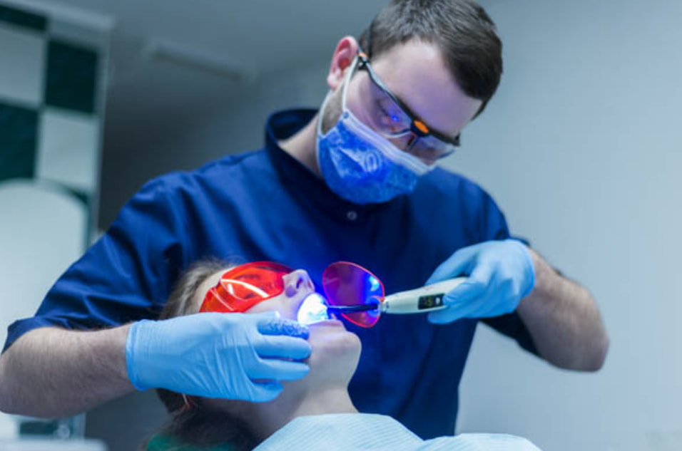 A man in a blue shirt and gloves receives a dental cleaning at a clinic, focusing on oral hygiene.