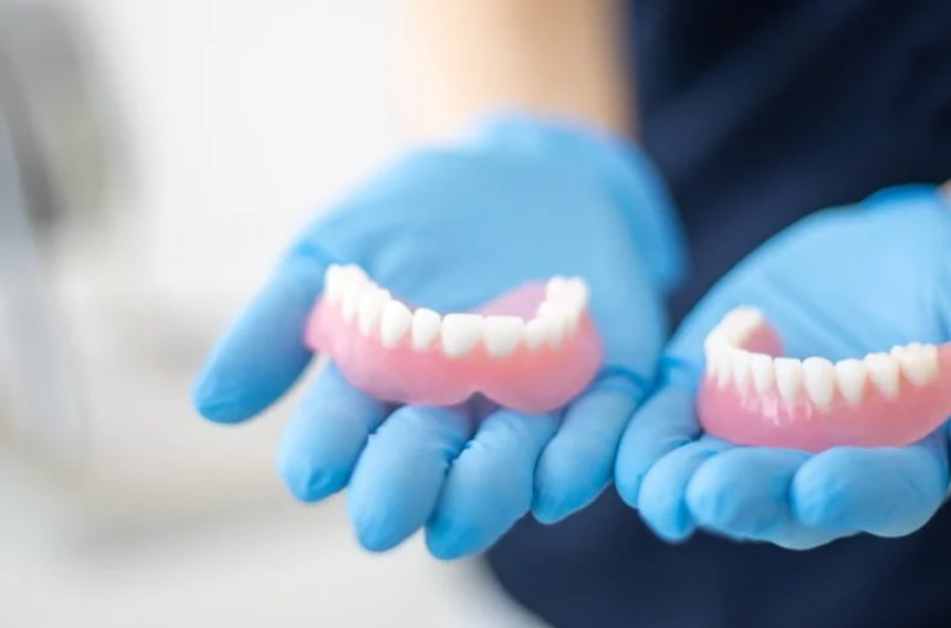 A person in blue gloves holds a tooth next to a pink tooth, showcasing dental care or a dental procedure. 