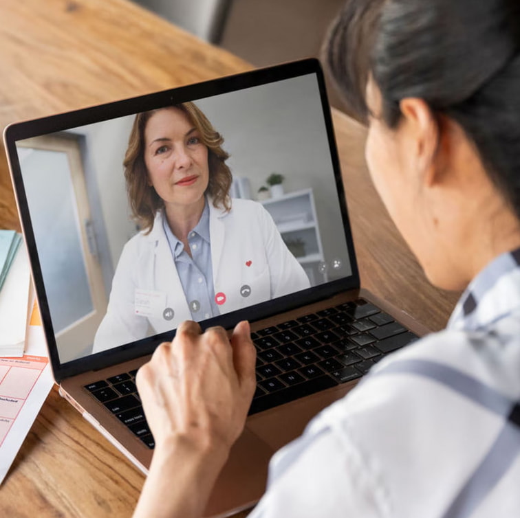 A woman video chatting with a doctor on her laptop, engaged in a virtual consultation from her home.