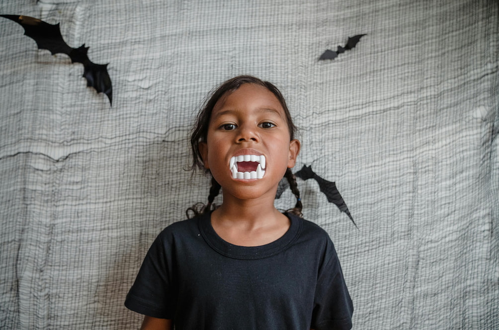 A little girl holds a toothbrush, smiling with bats illustrated on her teeth, showcasing a playful dental theme.