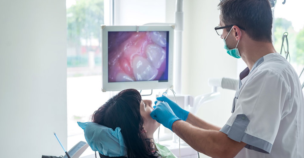 A man sits in a dental chair while a dentist examines his teeth with a dental tool.