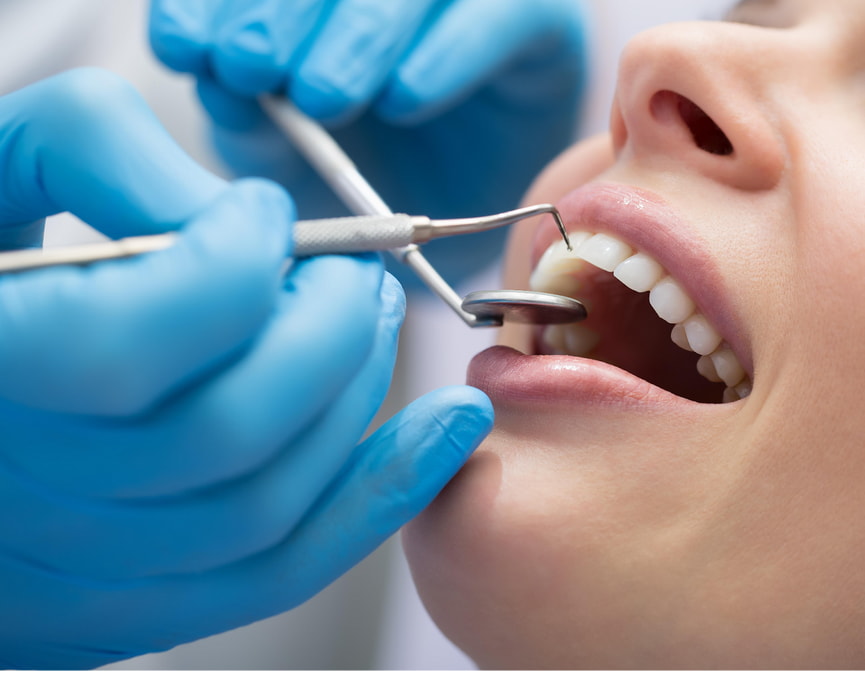 A woman sits in a dental chair while a dentist cleans her teeth with dental tools.