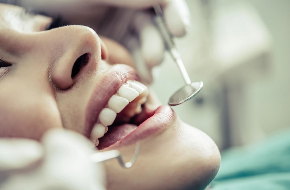 A woman sits in a dental chair while a dentist cleans her teeth with dental tools.