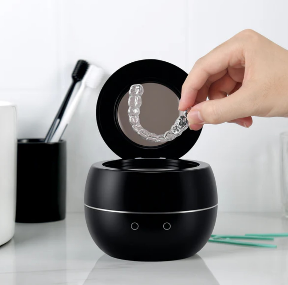 A person placing a tube of toothpaste into a toothbrush holder on a bathroom counter. 