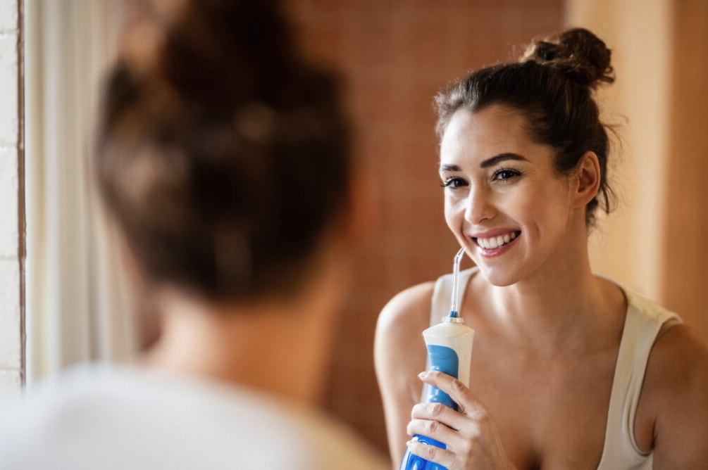 A woman is using an electric toothbrush to brush her teeth in a bright bathroom setting. 