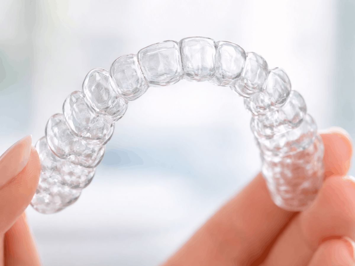 Close-up of a clear Invisalign-style aligner tray being held between fingers, used to straighten teeth discreetly