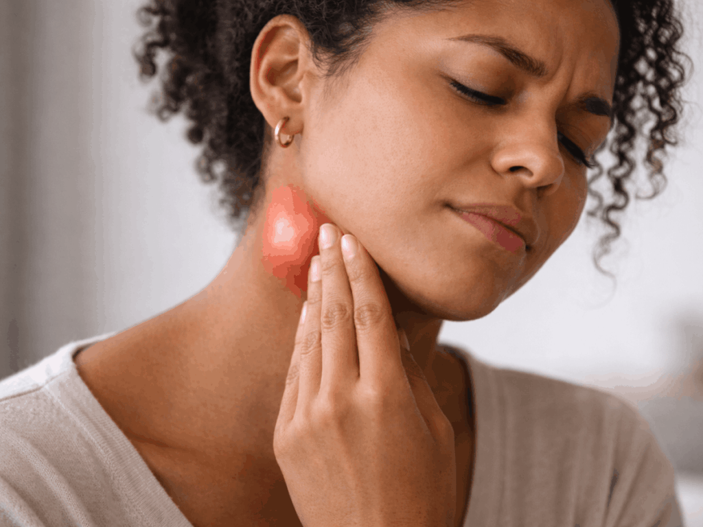 Photo of a woman touching the side of her neck with redness and swelling, showing a swollen lymph node near the jawline and neck tenderness