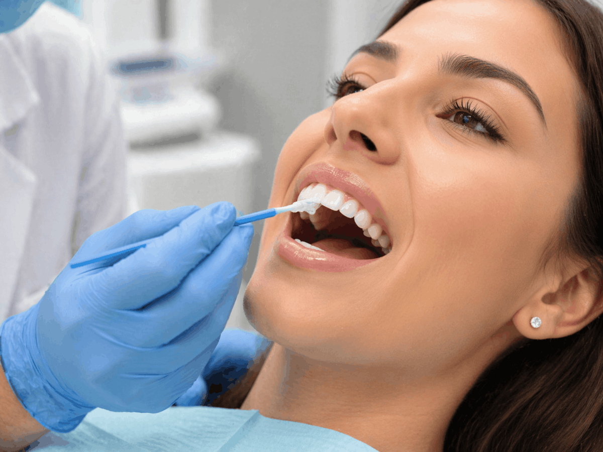 Dentist applying fluoride varnish to patient’s teeth during a professional dental treatment in clinic