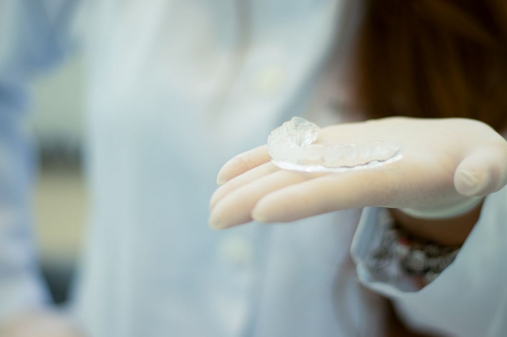 Gloved hand holds a clear dental aligner, showcasing orthodontic care in a clinical setting.