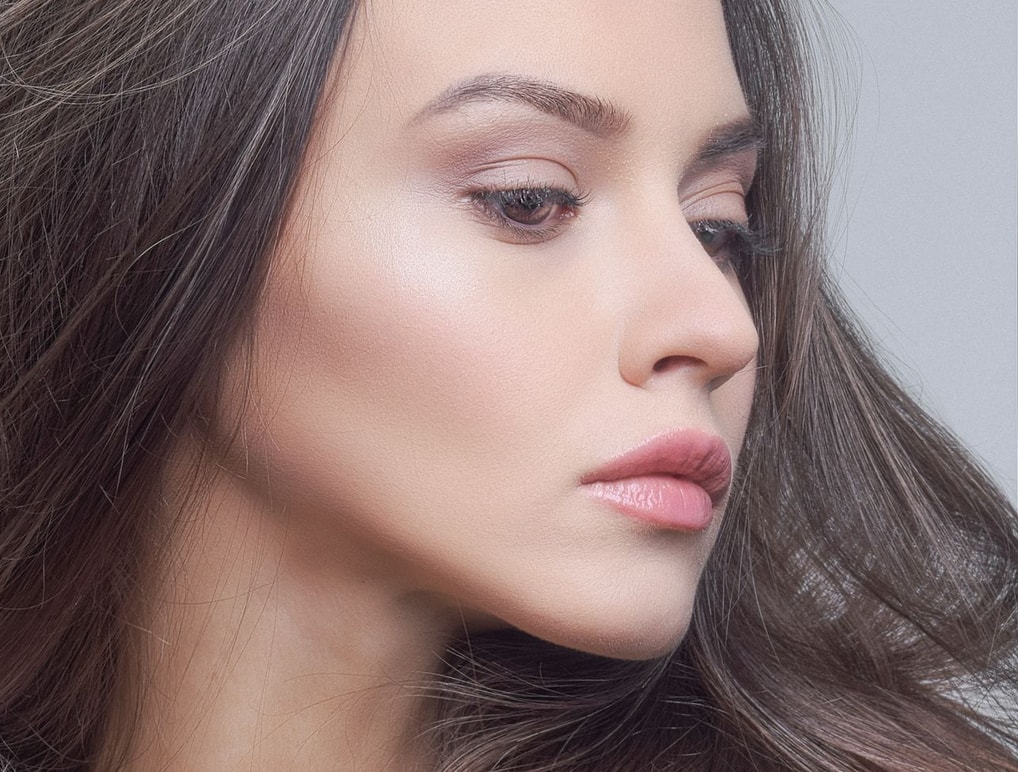 Close-up of a woman with long brown hair, showing a serene expression and smooth skin, gazing thoughtfully to the side.
