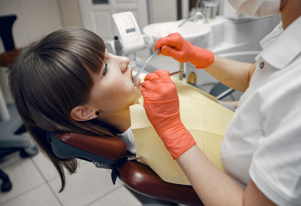 Dentist in red gloves examines a patient in a dental chair, using tools for a routine check-up in a modern clinic setting.
