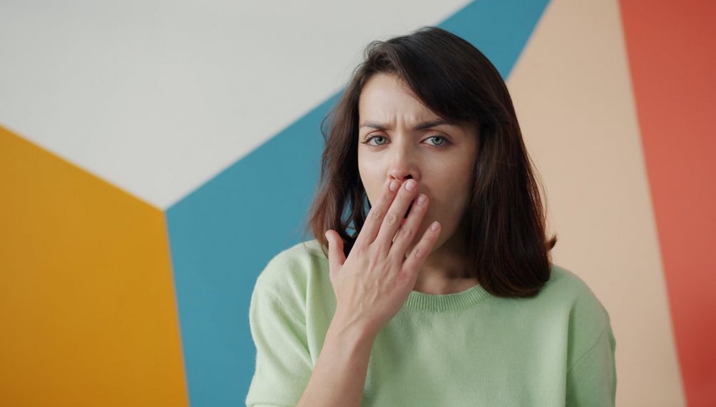 A woman in a green sweater yawns, covering her mouth, against a colorful geometric background of orange, blue, and beige.